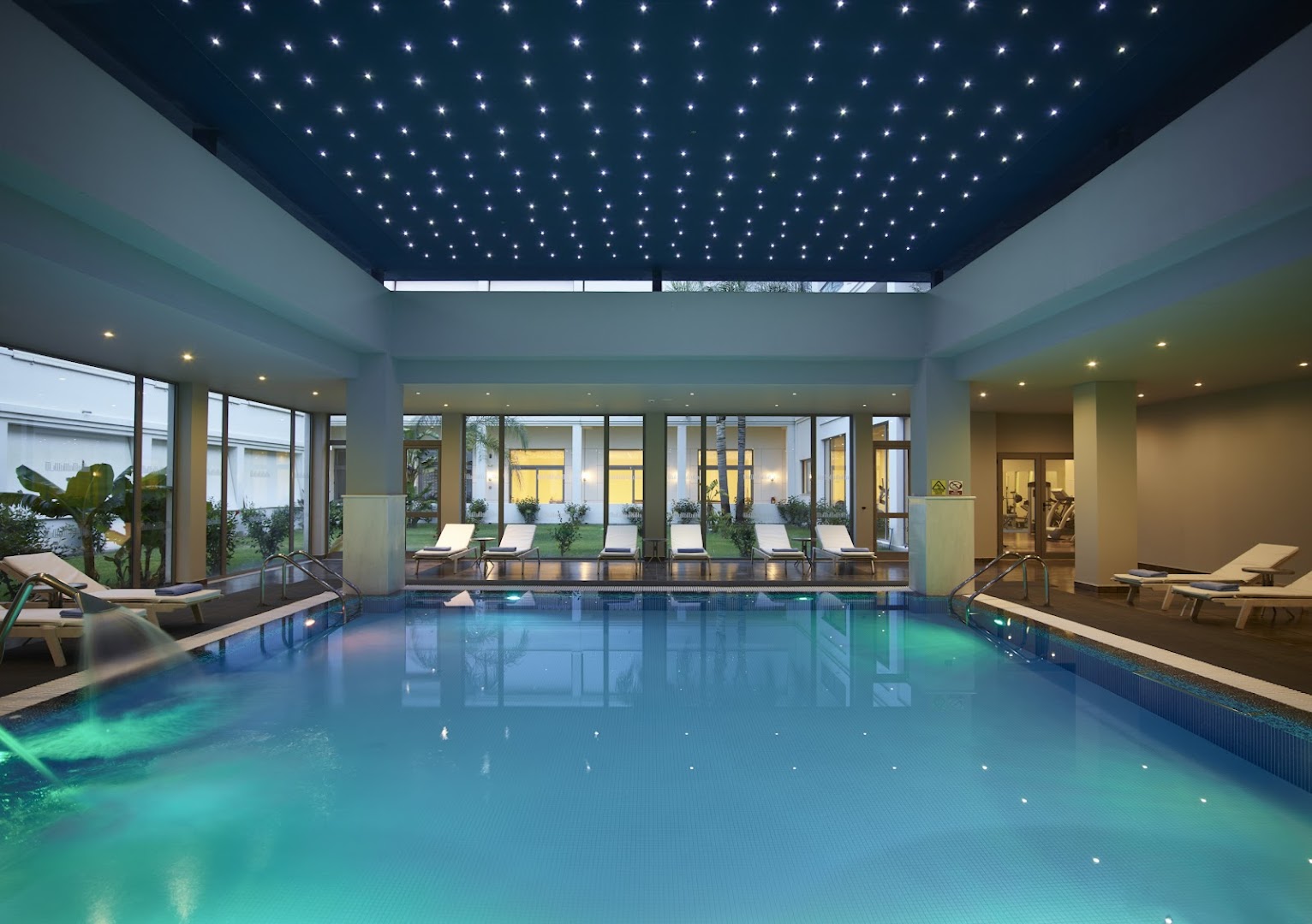 Apollo Blue Hotel iekštelpu baseins ar zvaigžņotu griestu apgaismojumu un atpūtas krēsliem — spa zona relaksācijai