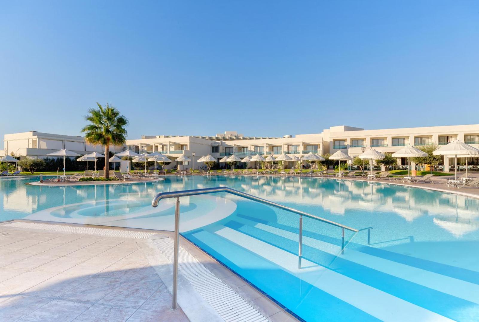 Apollo Blue Hotel modernā arhitektūra un galvenais baseins ar pakāpieniem — gaiši viesnīcas numuri ar balkoniem un saulessargi