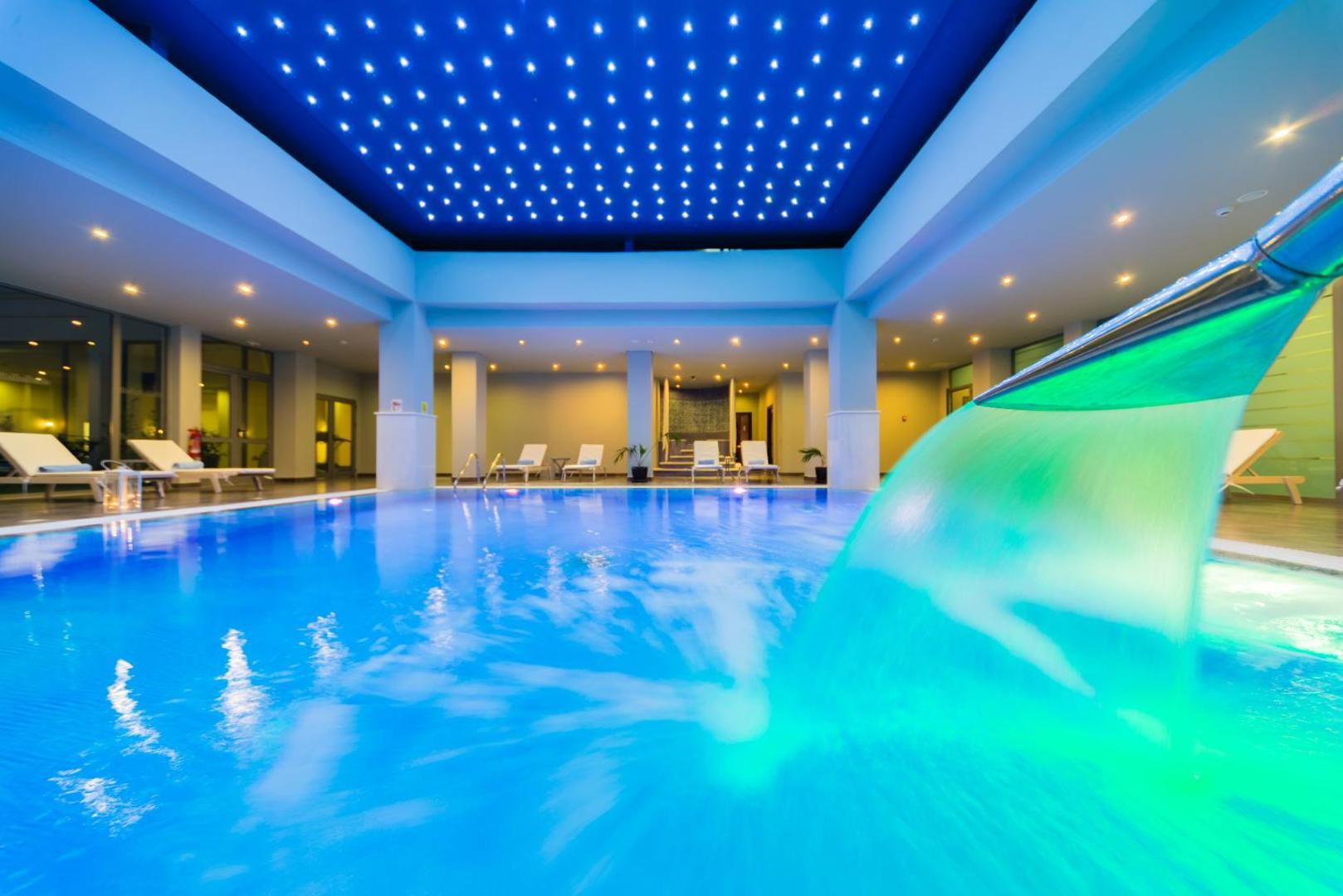 Apollo Blue Hotel iekštelpu baseins ar kaskādi un zvaigžņotu griestu apgaismojumu Rodas salā, Grieķijā — relaksācijas zona ar atpūtas krēsliem
