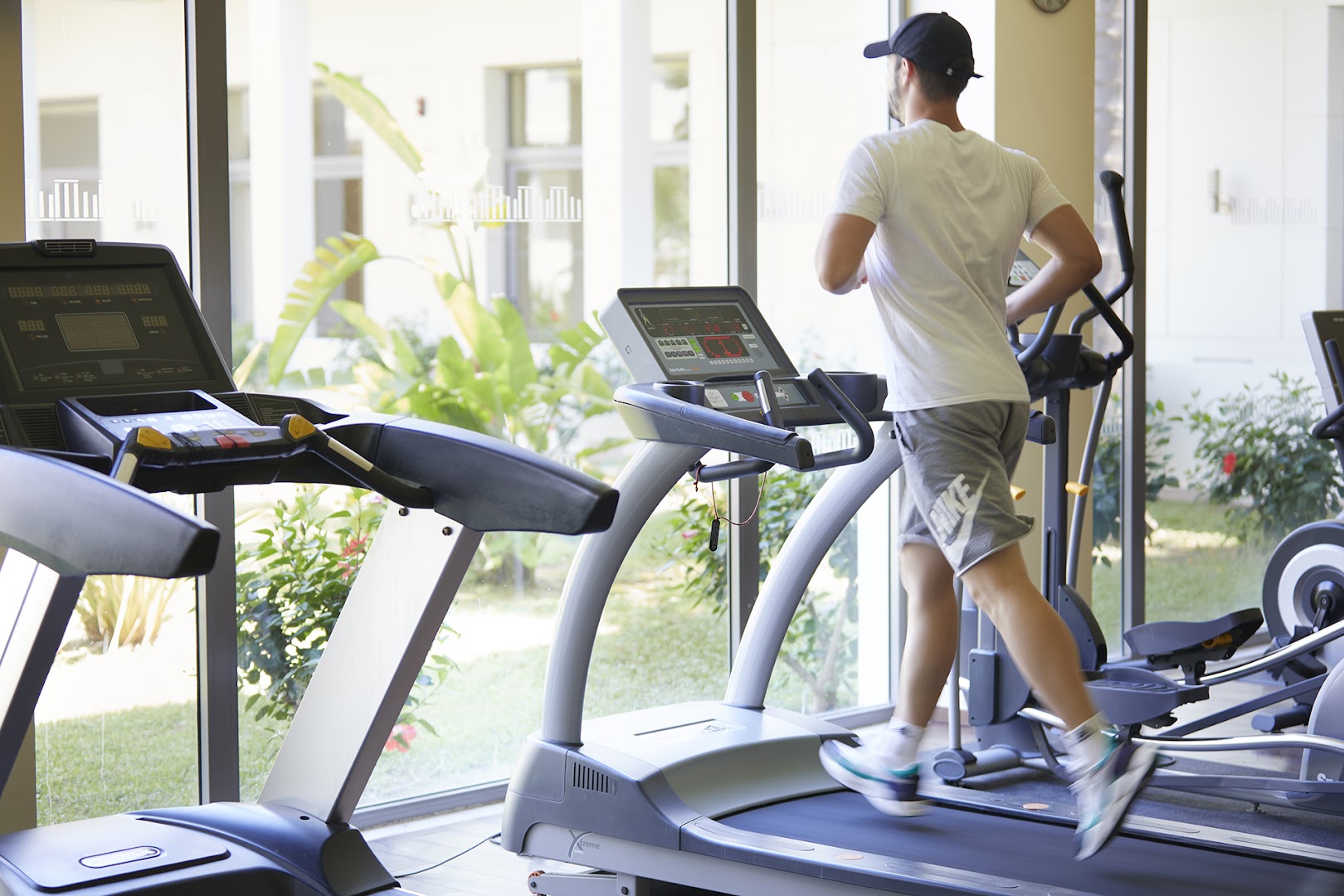 Apollo Blue Hotel fitnesa centrs ar skrejceliņiem un skatu uz dārzu caur lielajiem logiem — mūsdienīgs aprīkojums aktīvai atpūtai