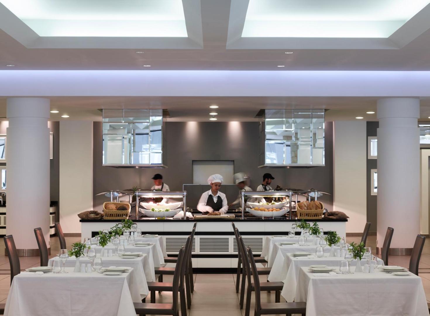 Princess Andriana Resort & Spa galvenais restorāns Rodas salā — bufetes zona ar pavāriem un eleganti klātiem galdiem vakariņām