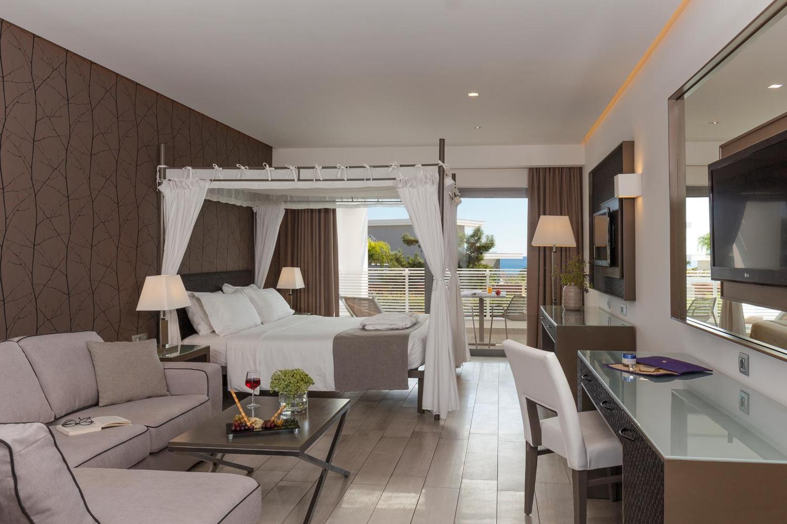 Elegants Princess Andriana Resort & Spa numurs ar atpūtas zonu, lielu gultu un skatu uz jūru tālumā
