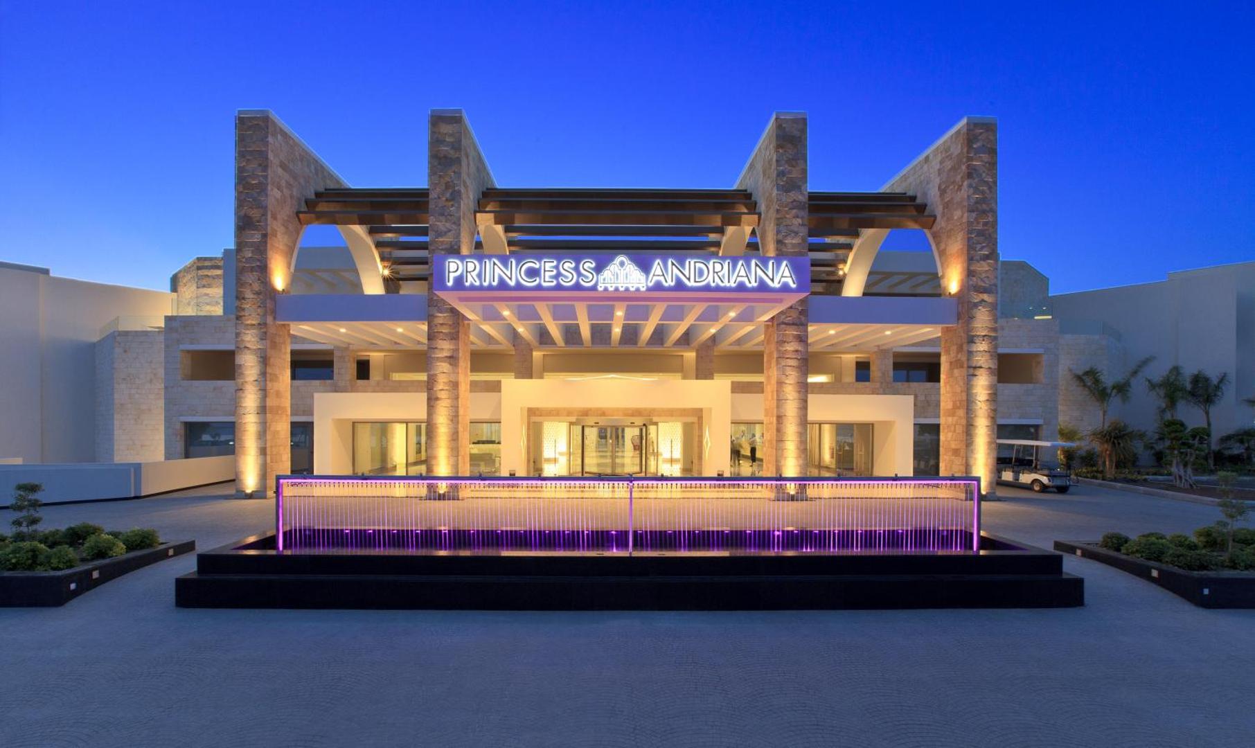 Princess Andriana Resort & Spa galvenā ieeja un vestibila fasāde ar modernu apgaismojumu un strūklaku vakarā