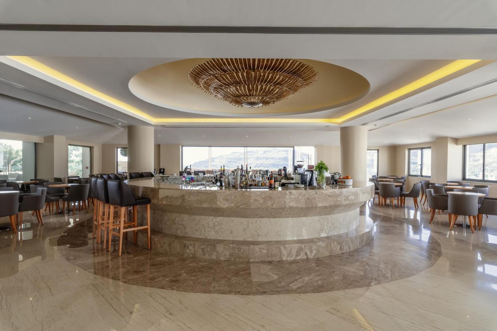 Lindos Village Resort & Spa modernais bārs ar apaļu leti un panorāmas logiem uz Rodas salas kalnaino ainavu