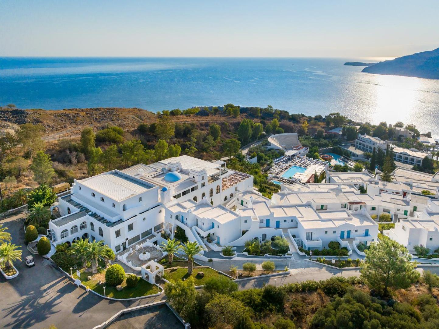 Lindos Village Resort & Spa aerofoto skats uz balto ēku kompleksu un baseiniem Rodas salā pie zilās Vidusjūras piekrastes