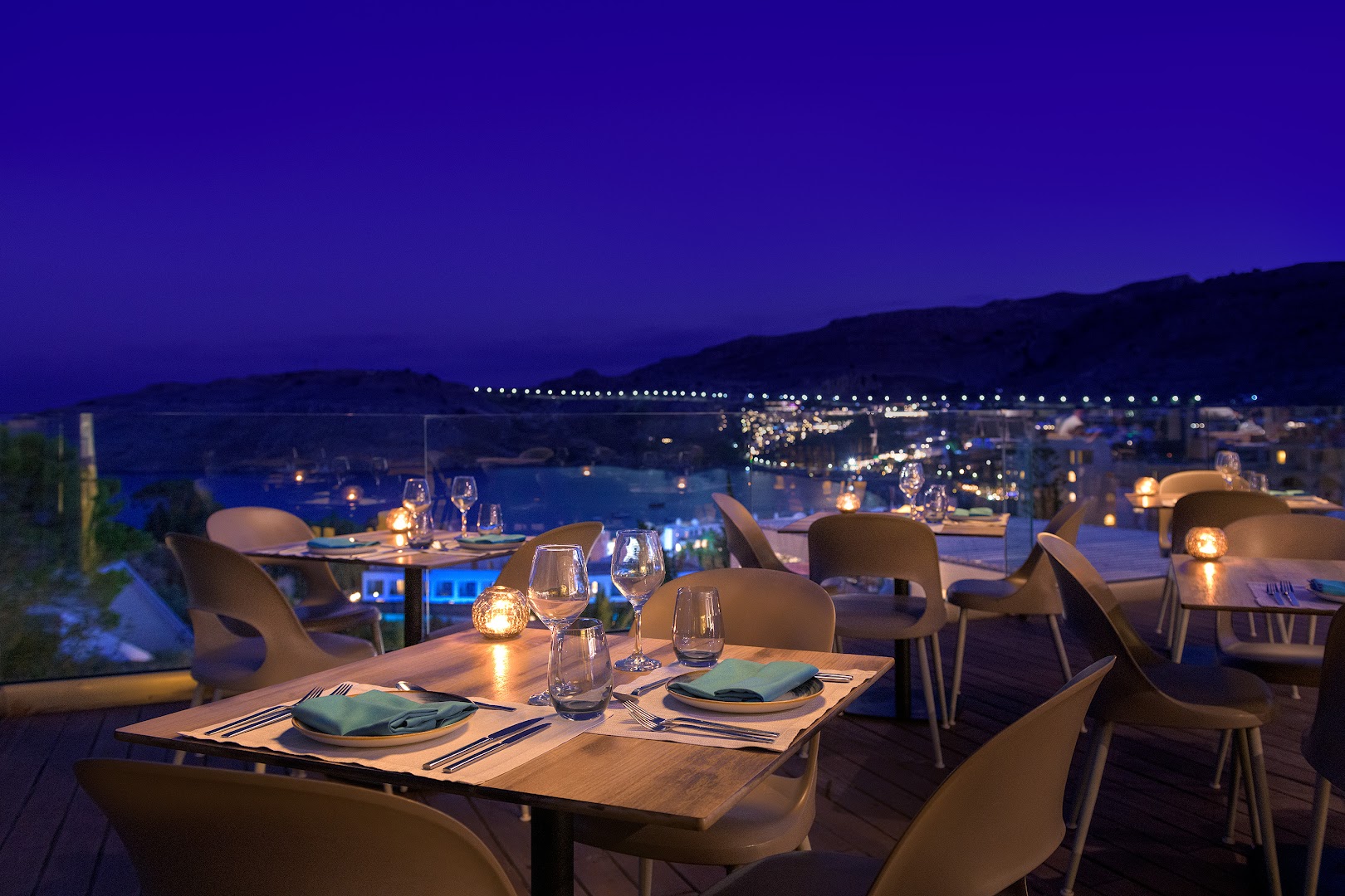 Lindos Village Resort & Spa restorāna terase vakarā ar izgaismotiem galdiem un skatu uz naksnīgo pilsētu