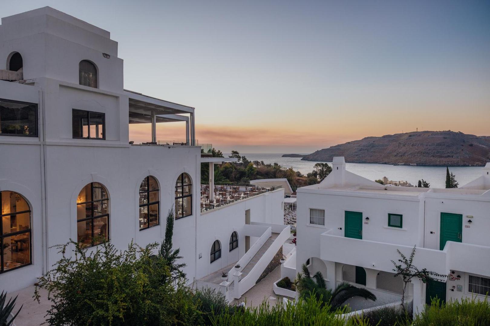 Lindos Village Resort & Spa terase ar skatu uz jūru un kalniem saulrieta laikā, baltas arhitektūras detaļas Rodas salā