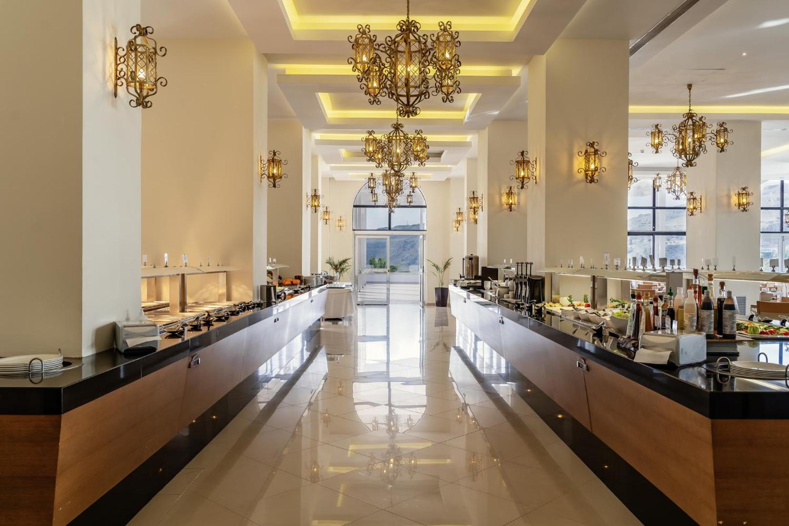 Lindos Village Resort & Spa galvenā restorāna bufetes zona ar greznām lustrām un plašu ēdienu izvēli
