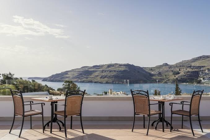 Lindos Village Resort & Spa āra terase ar galdiņiem un skatu uz Vidusjūras līci Rodas salā Grieķijā