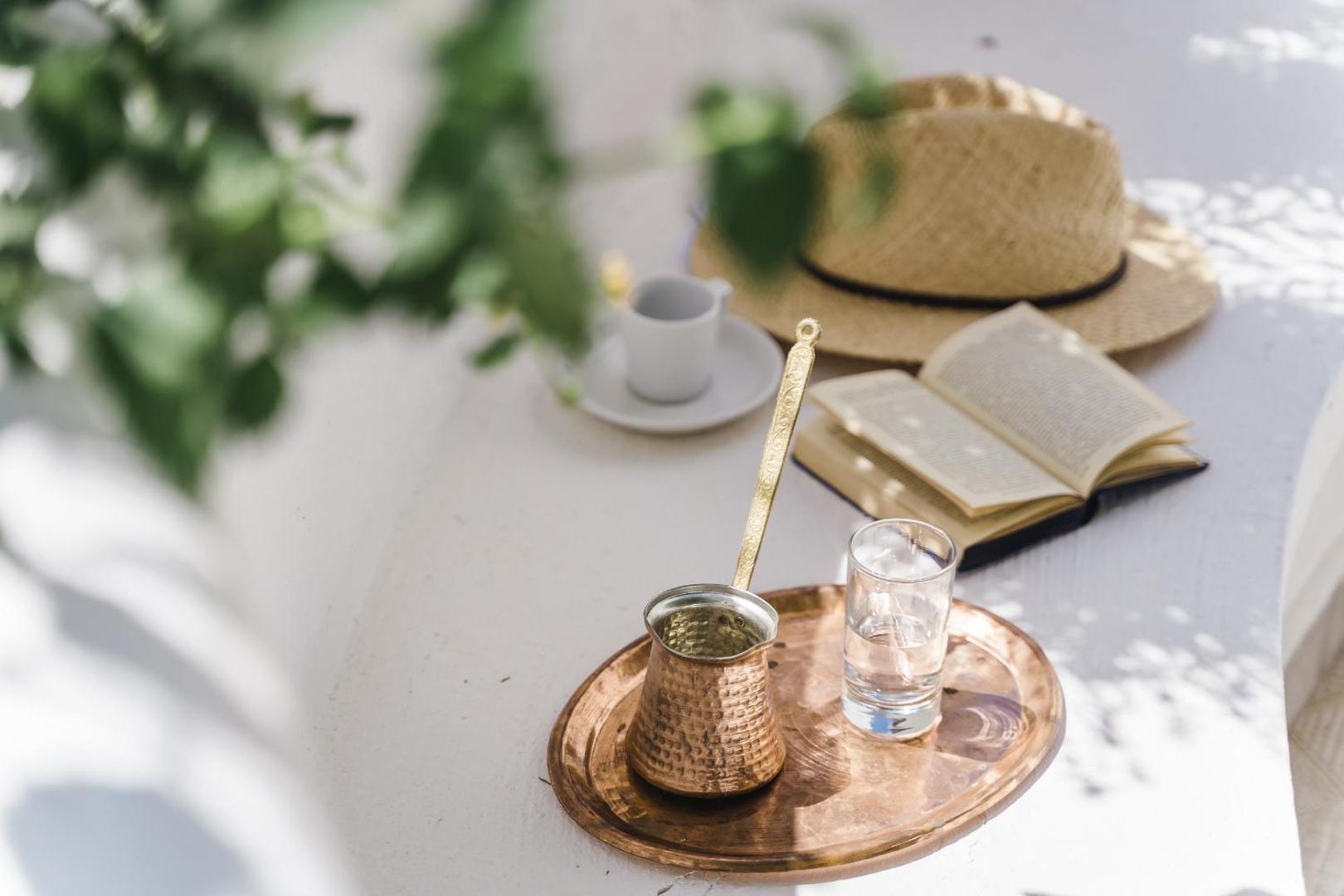 Grieķu kafija vara traukā uz paplātes Lindos Village Resort & Spa — rīta kafija ar grāmatu un salmu cepuri