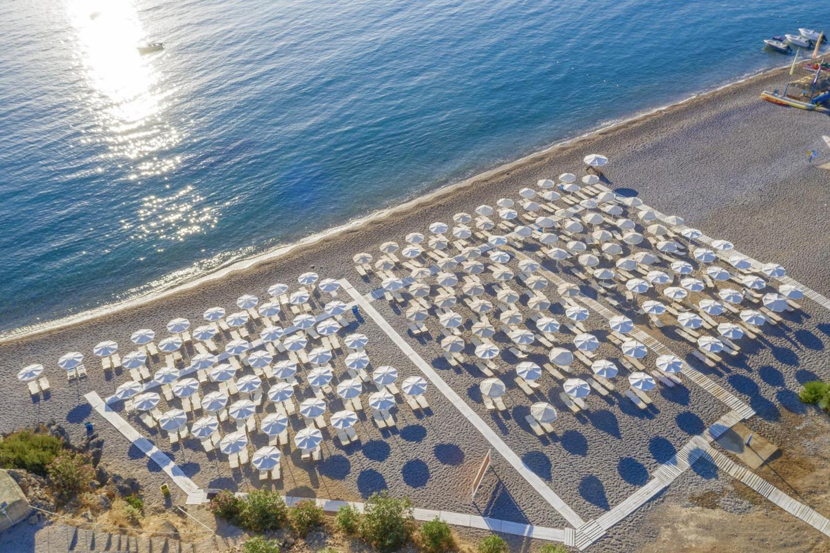 Lindos Village Resort & Spa privātā pludmale ar daudziem baltiem saulessargiem un zviļņiem Rodas piekrastē