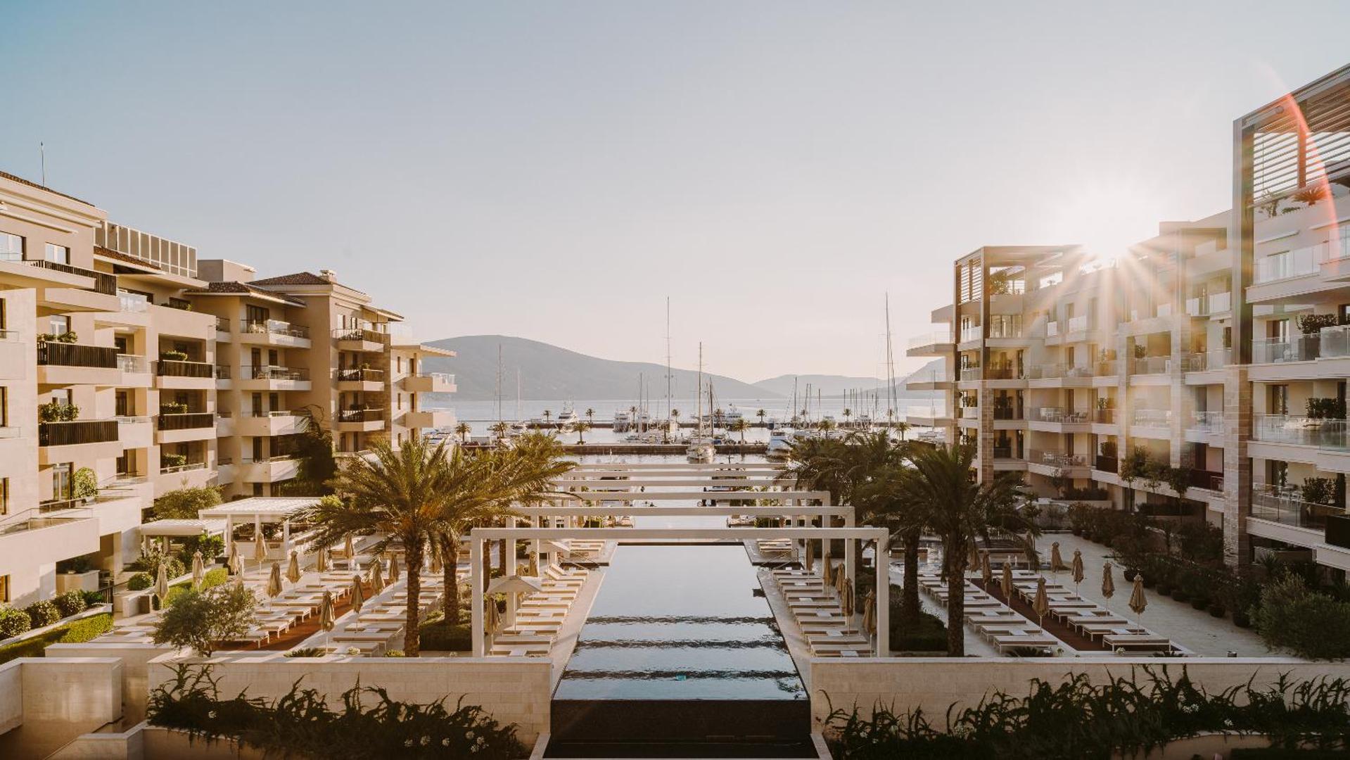 Regent Porto Montenegro kūrorta arhitektūra un baseina zona saules staros ar skatu uz līci un jahtām