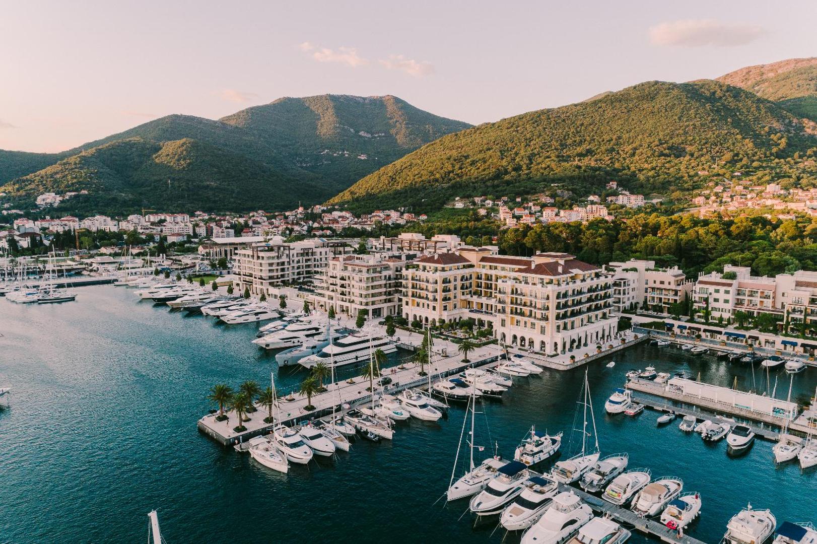 Regent Porto Montenegro viesnīcas ēkas un jahtu piestātne Tivatas līcī Melnkalnē — skats no putna lidojuma uz piekrasti un kalniem