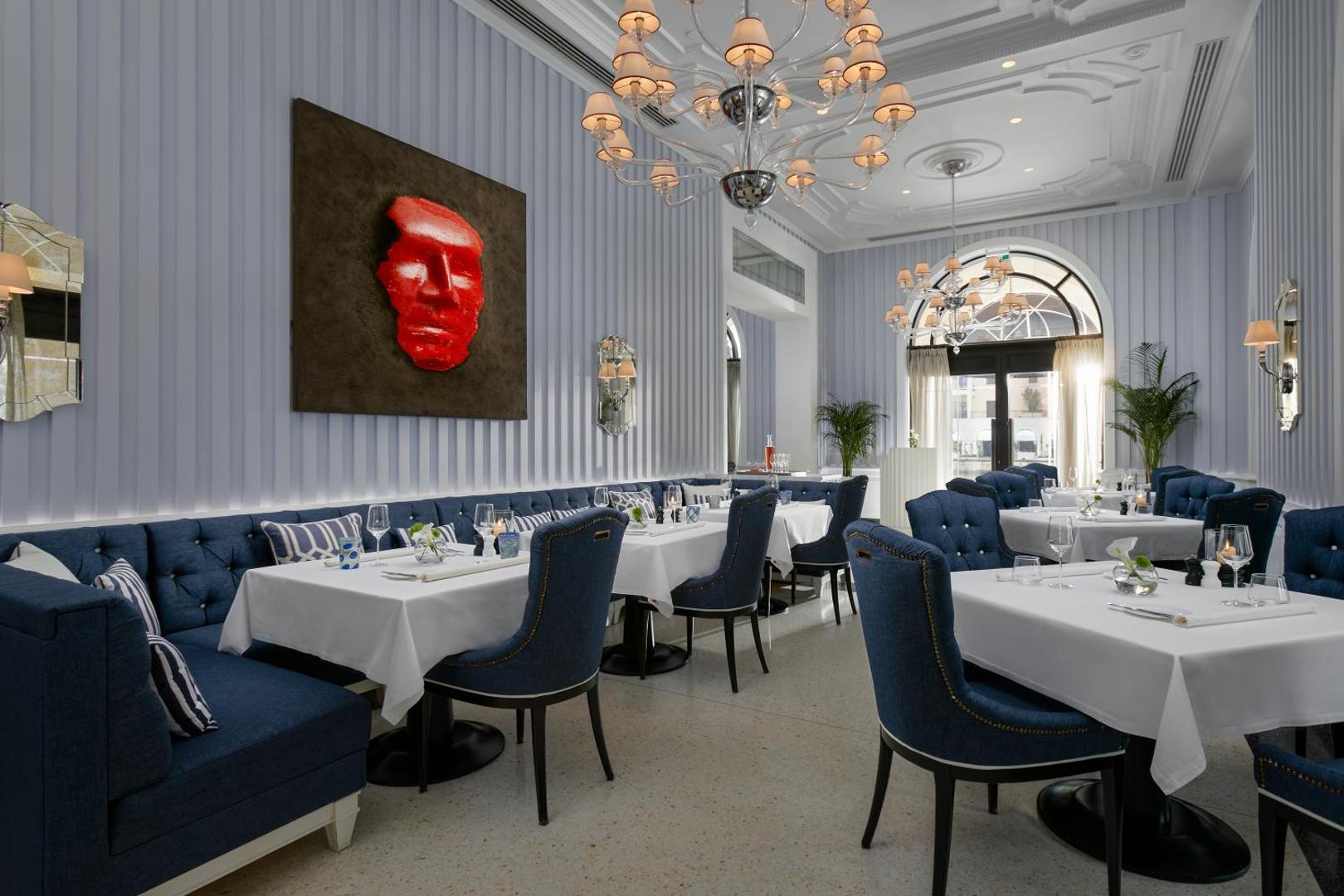 Regent Porto Montenegro elegants restorāns ar ziliem samta krēsliem, baltiem galdautiem un modernu mākslas darbu pie sienas