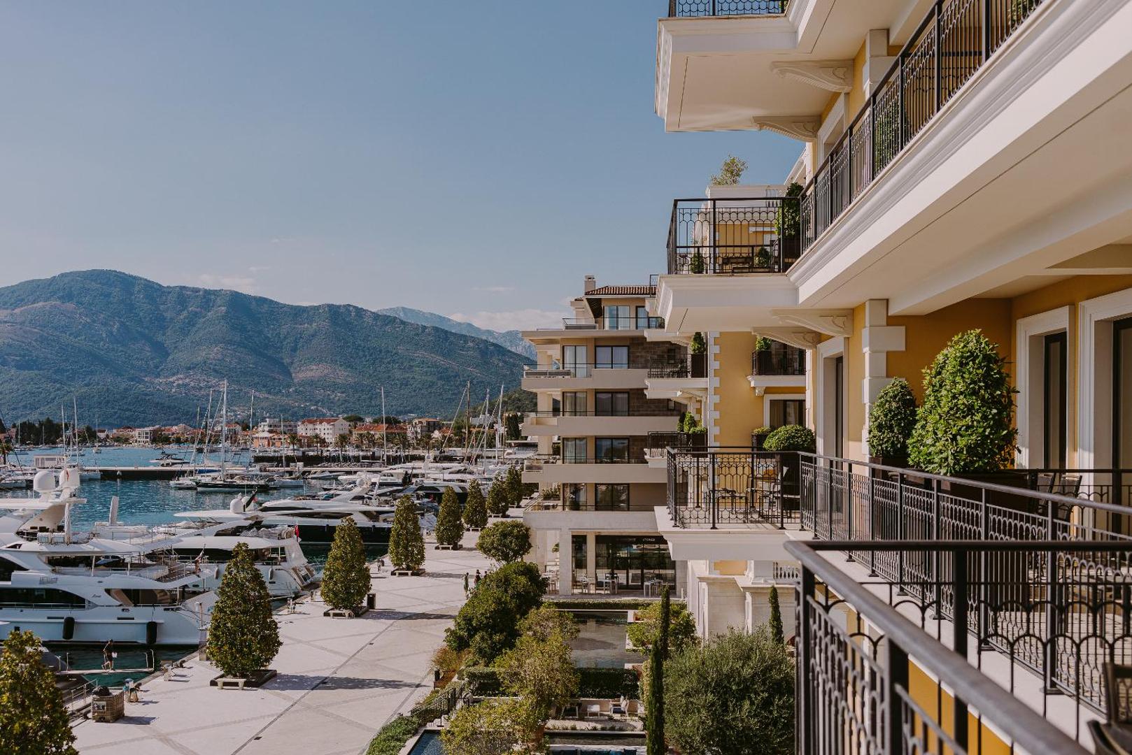 Regent Porto Montenegro viesnīcas fasāde un balkoni ar skatu uz jahtu piestātni un kalniem Tivatas līcī