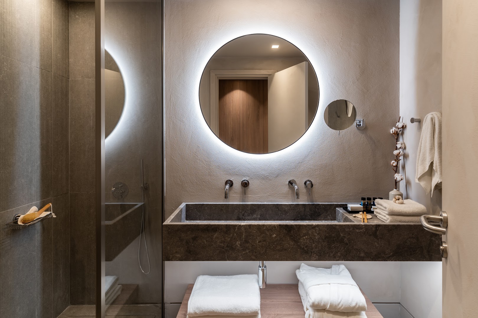 Luksusa numura vannasistaba Elissa Lifestyle Resort viesnīcā Rodā — tumša akmens izlietne, izgaismots spogulis un mīksti halāti