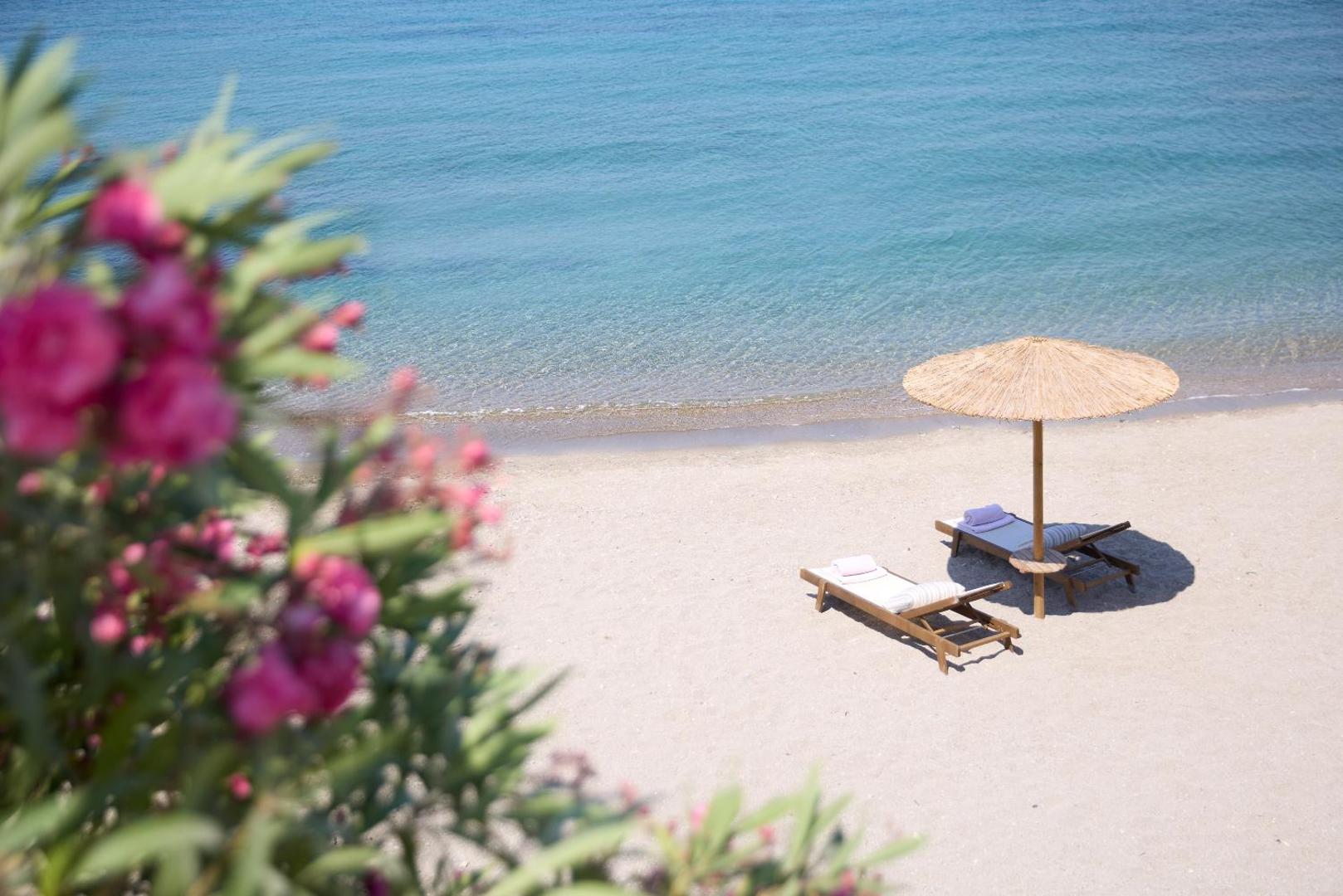 Elissa Lifestyle Resort privātā smilšu pludmale Rodas salā ar diviem koka sauļošanās krēsliem un salmu saulessargu pie dzidra jūras ūdens
