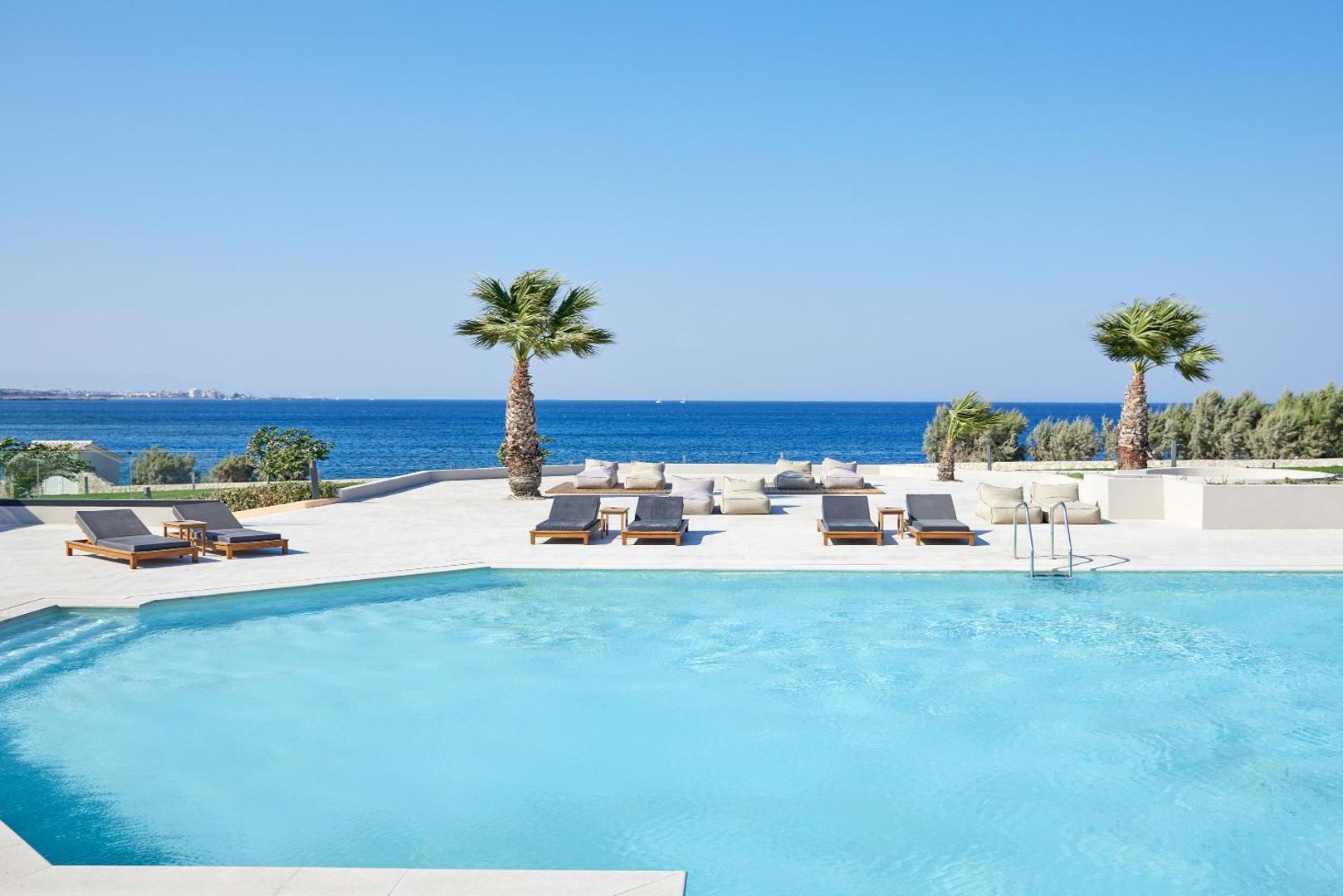 Elissa Lifestyle Resort galvenais baseins piekrastē ar palmām un sauļošanās krēsliem — skats uz Vidusjūru Rodas salā