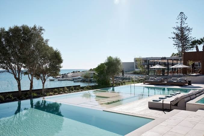 Elissa Lifestyle Resort baseins ar pārplūdes malu un atpūtas zonu ūdenī — skats uz jūru un olīvkokiem Rodā