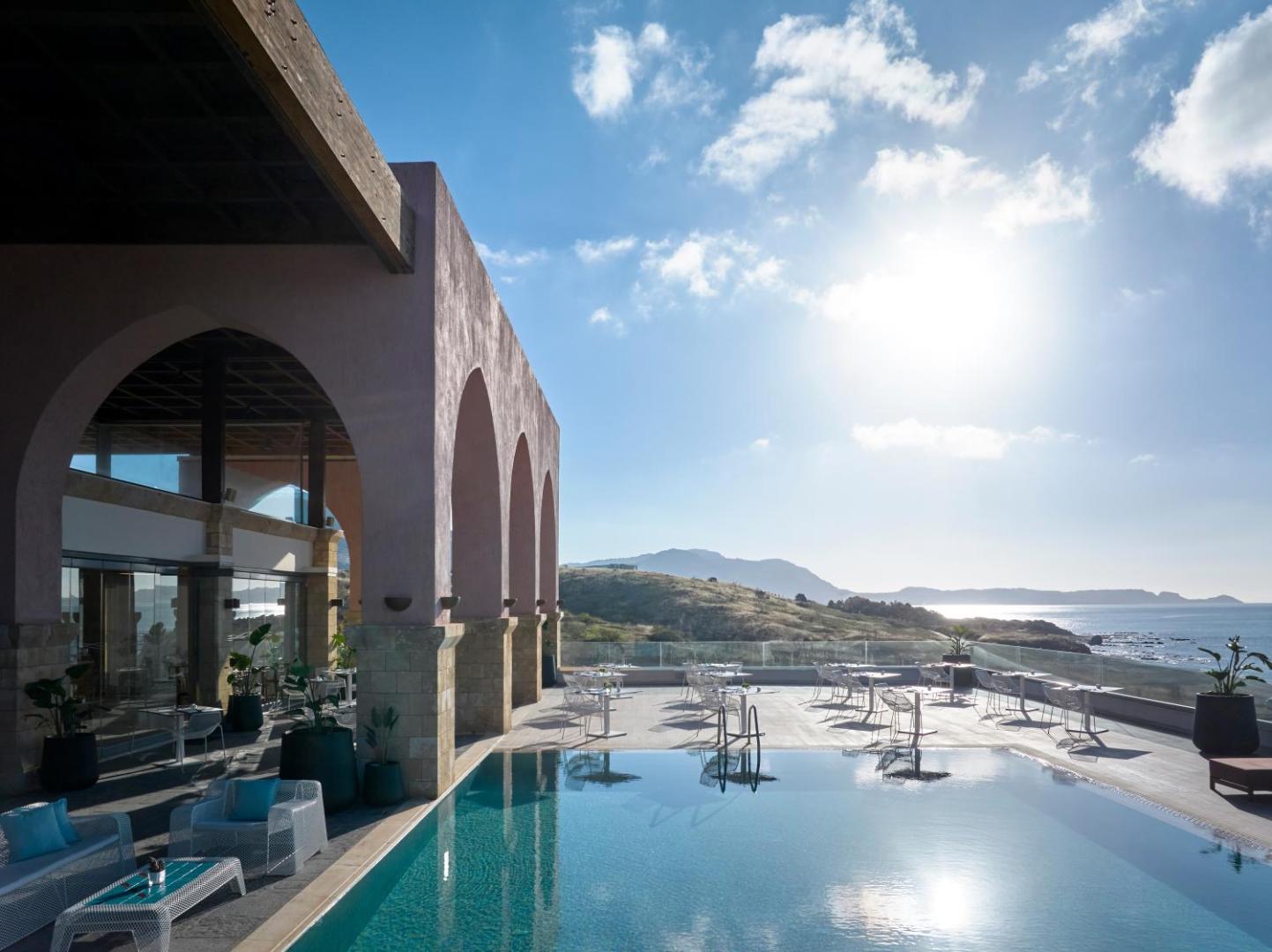 Boutique 5 Hotel & Spa āra terase ar baseinu un skatu uz kalniem Rodas salā — saulaina atpūtas zona ar galdiņiem