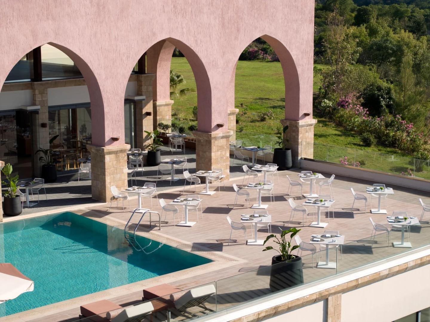 Boutique 5 Hotel & Spa āra restorāna terase pie baseina ar baltiem galdiem un krēsliem zem rozā arkām Rodas piekrastē