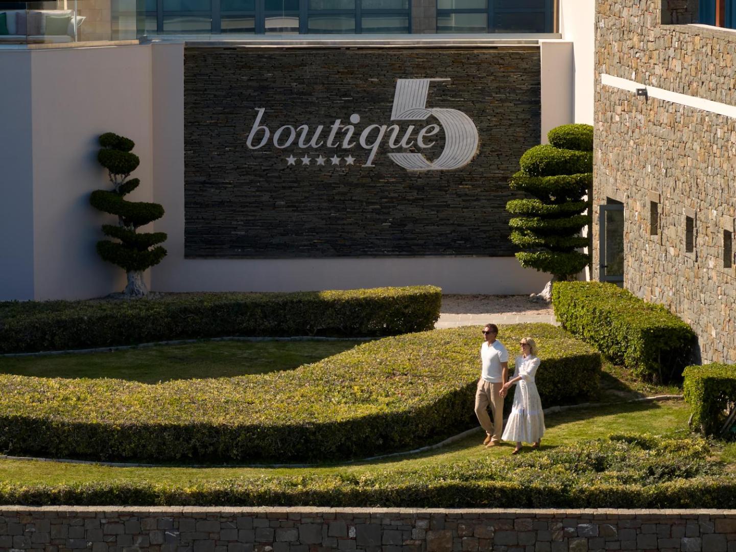 Pāris pastaigājas pa Boutique 5 Hotel & Spa koptajiem dārziem pie viesnīcas logo sienas Rodas salā