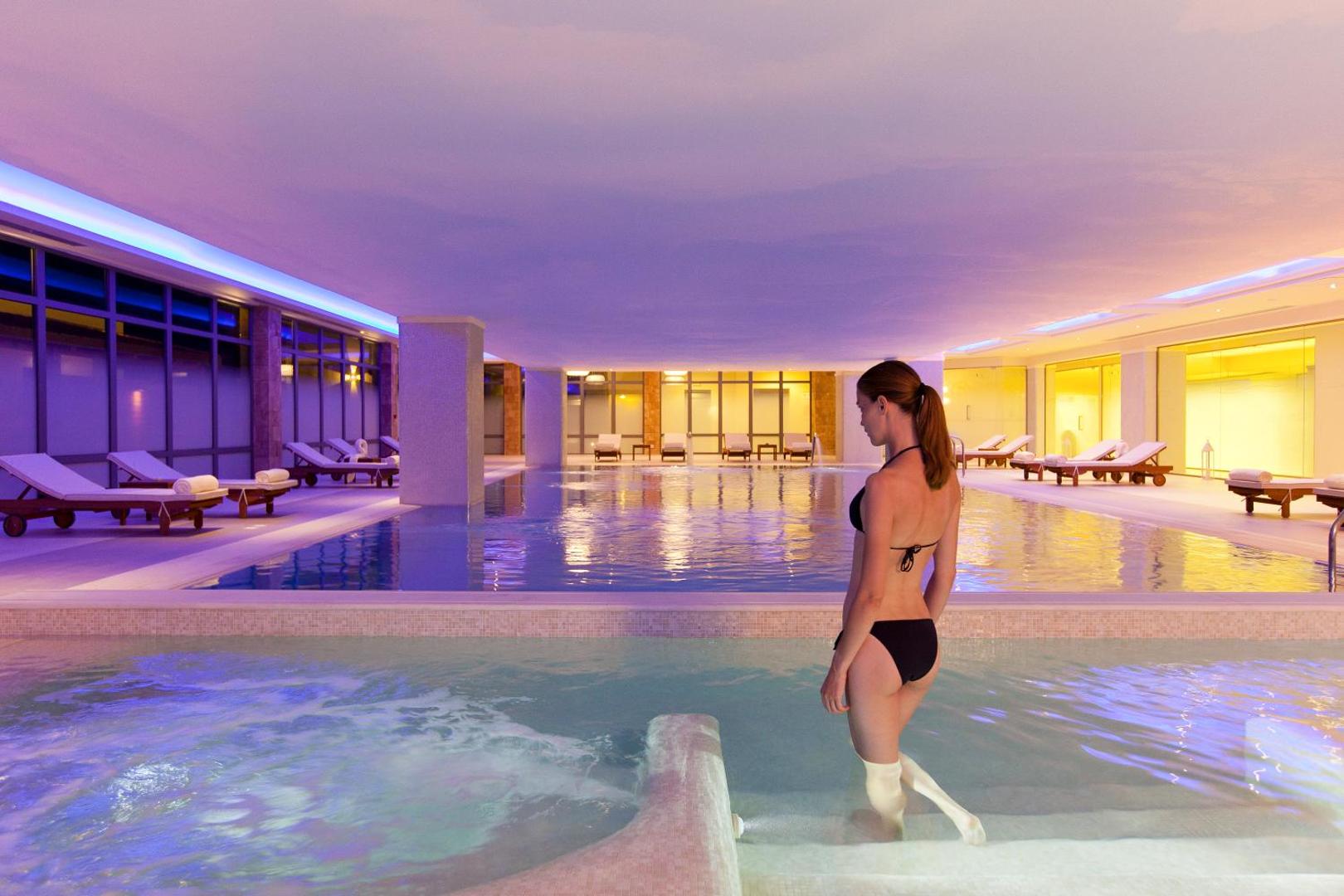 Boutique 5 Hotel & Spa iekštelpu baseins ar džakuzi zonu Rodas salā — sieviete kāpj ūdenī, apkārt atpūtas krēsli