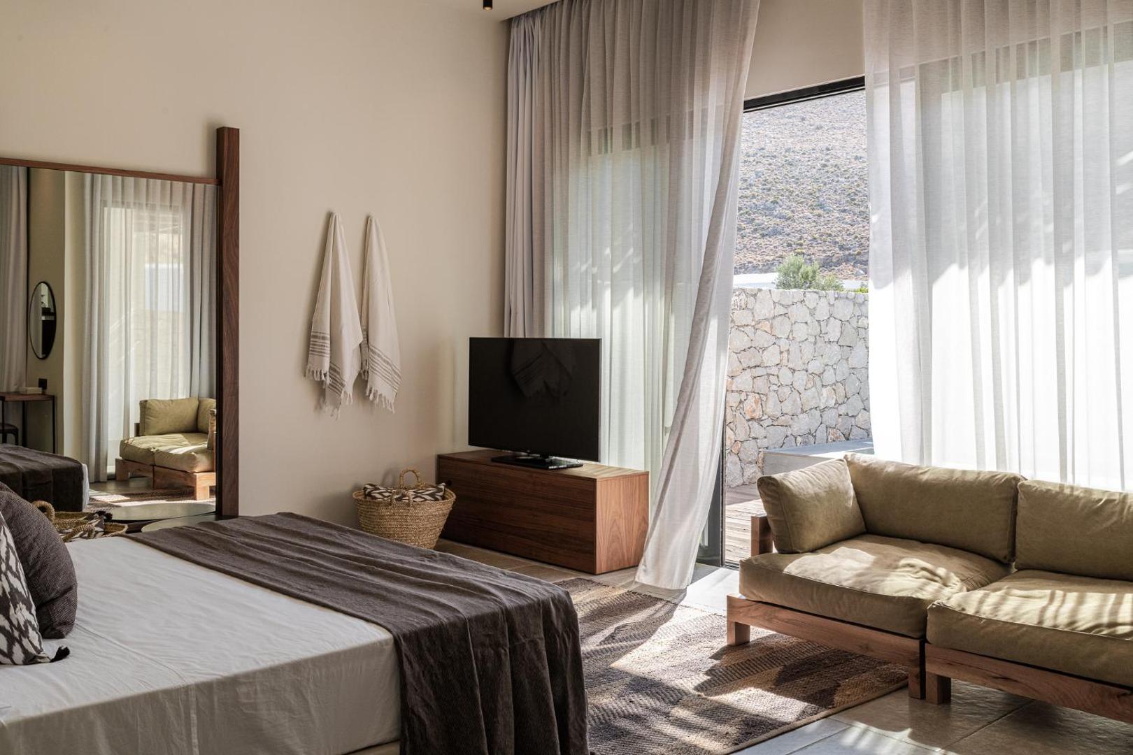 Casa Cook Rhodes numura interjers ar atpūtas zonu, dīvānu un skatu uz kalnaino ainavu caur atvērtām terases durvīm
