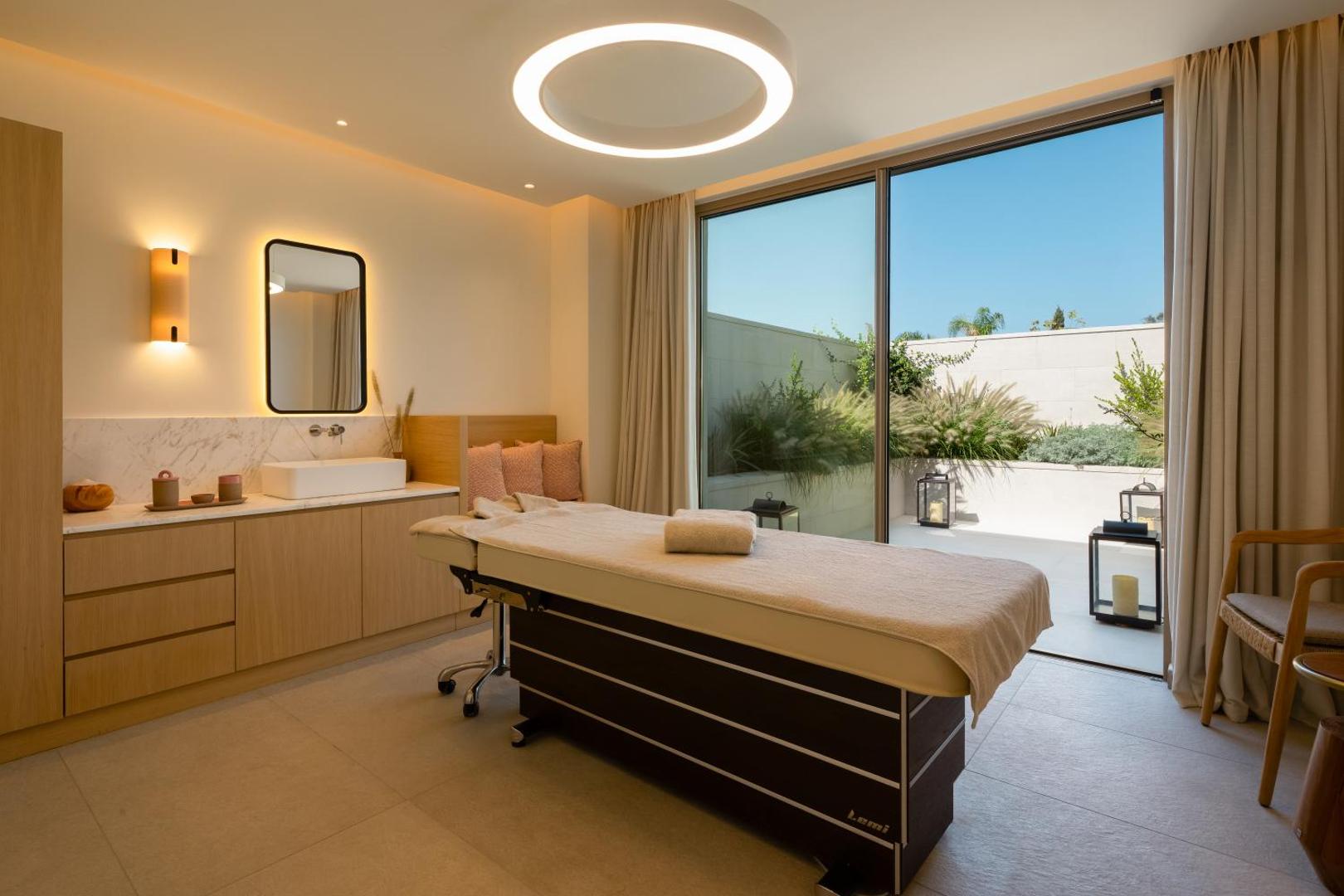 Mitsis Faliraki Beach Hotel & Spa moderns spa procedūru numurs ar masāžas galdu un skatu uz privātu dārza terasi