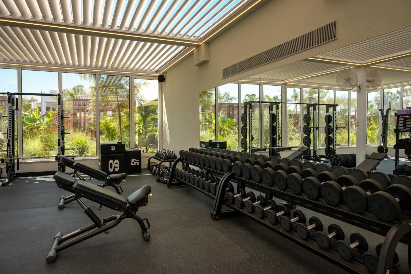 Mitsis Faliraki Beach Hotel & Spa moderns fitness centrs ar plašu hanteļu klāstu un skatu uz dārzu caur lieliem logiem