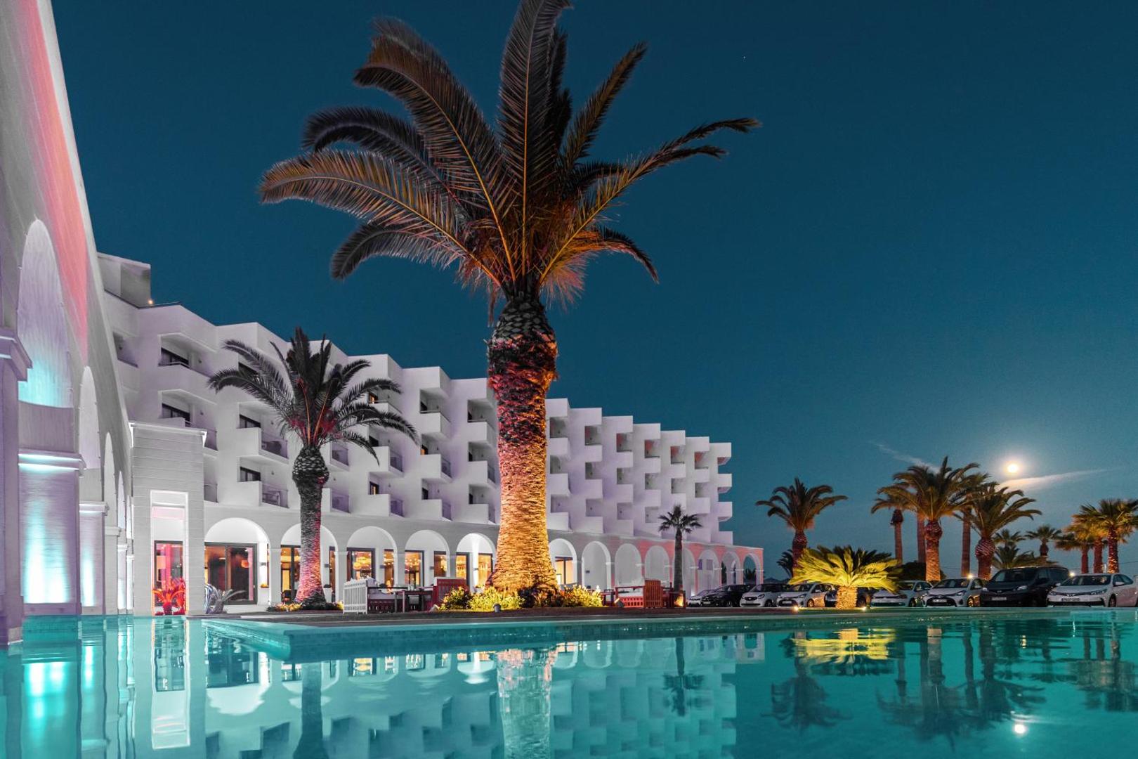 Mitsis Faliraki Beach Hotel & Spa fasāde vakarā ar izgaismotu baseinu un palmām Rodas salā, Grieķijā