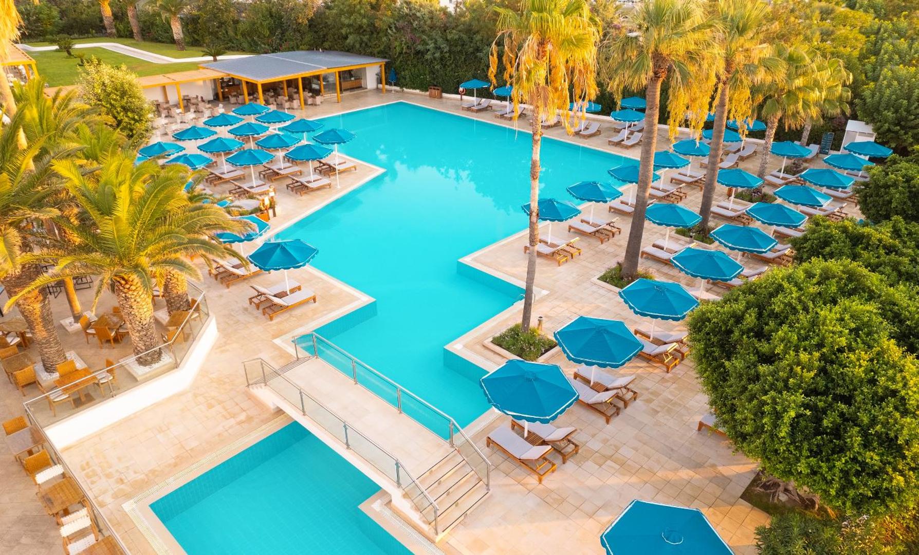 Mitsis Faliraki Beach Hotel & Spa baseina zona no augšas Rodas salā — daudz zilu saulessargu, sauļošanās krēsli un palmas