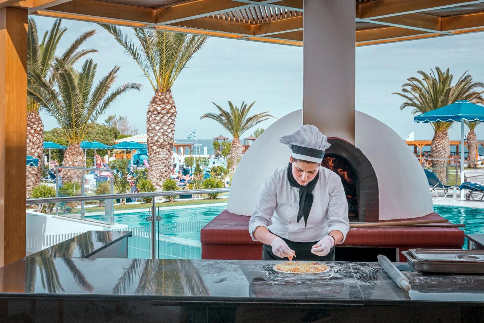 Mitsis Faliraki Beach Hotel & Spa pavārs gatavo picu malkas krāsnī āra restorānā pie baseina un palmām