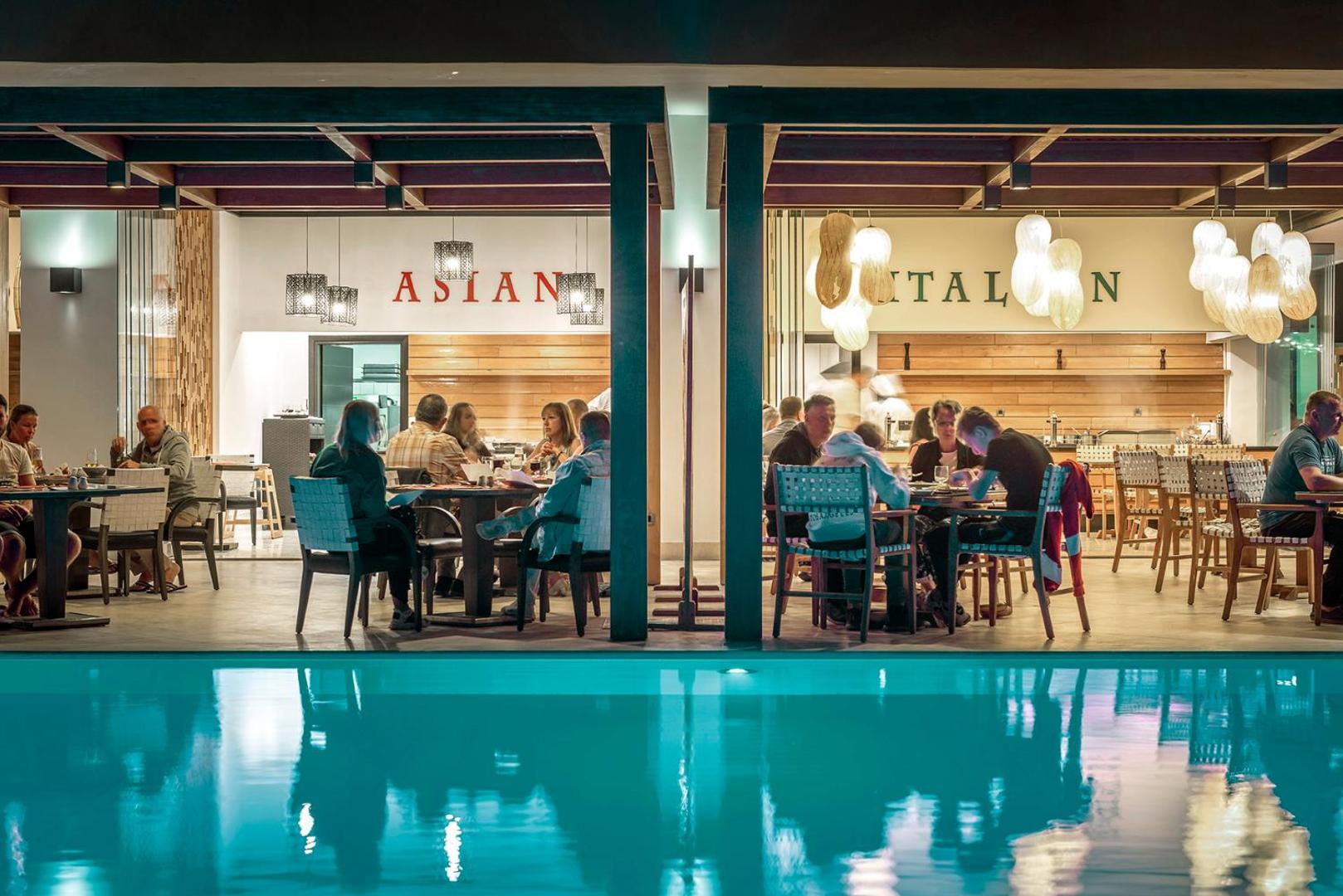 Mitsis Faliraki Beach Hotel & Spa tematiskie restorāni vakarā pie izgaismota baseina ar viesiem, kas bauda vakariņas