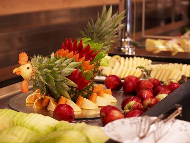 Mitsis Faliraki Beach Hotel & Spa bufetes restorāna augļu izlase ar mākslinieciski grieztu ananasu gaiļa formā
