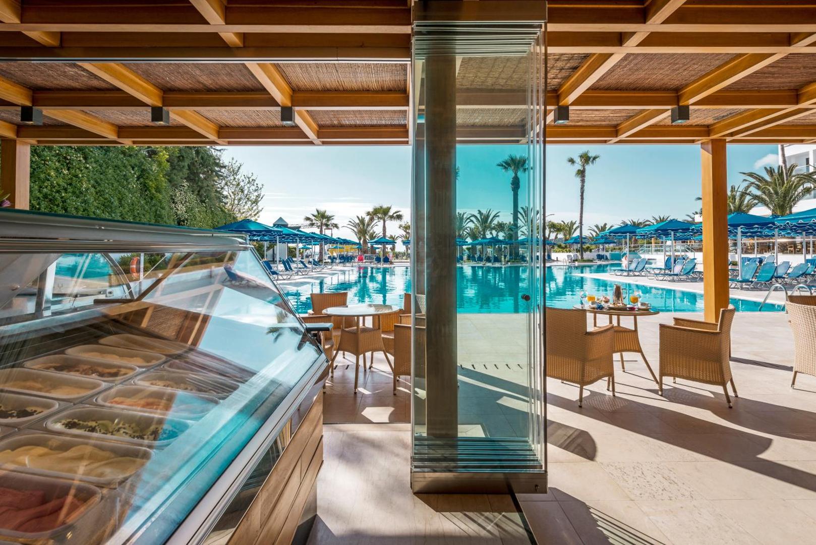 Mitsis Faliraki Beach Hotel & Spa saldējuma bārs un kafejnīca ar skatu uz lielo āra baseinu un ziliem saulessargiem