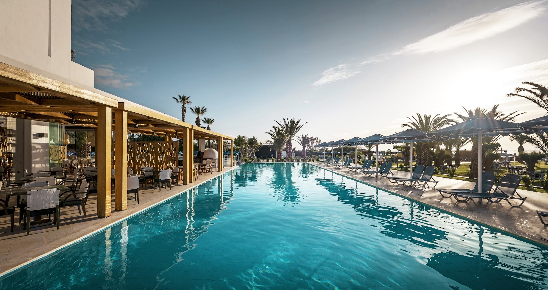 Mitsis Faliraki Beach Hotel & Spa garais peldbaseins pie restorāna terases Rodas salā — skats uz palmām un saulrieta gaismu
