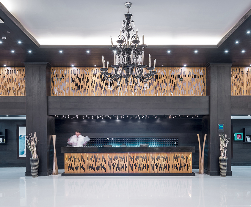 Mitsis Faliraki Beach Hotel & Spa recepcijas lete ar dekoratīviem koka paneļiem un greznu lustru viesnīcas galvenajā ēkā