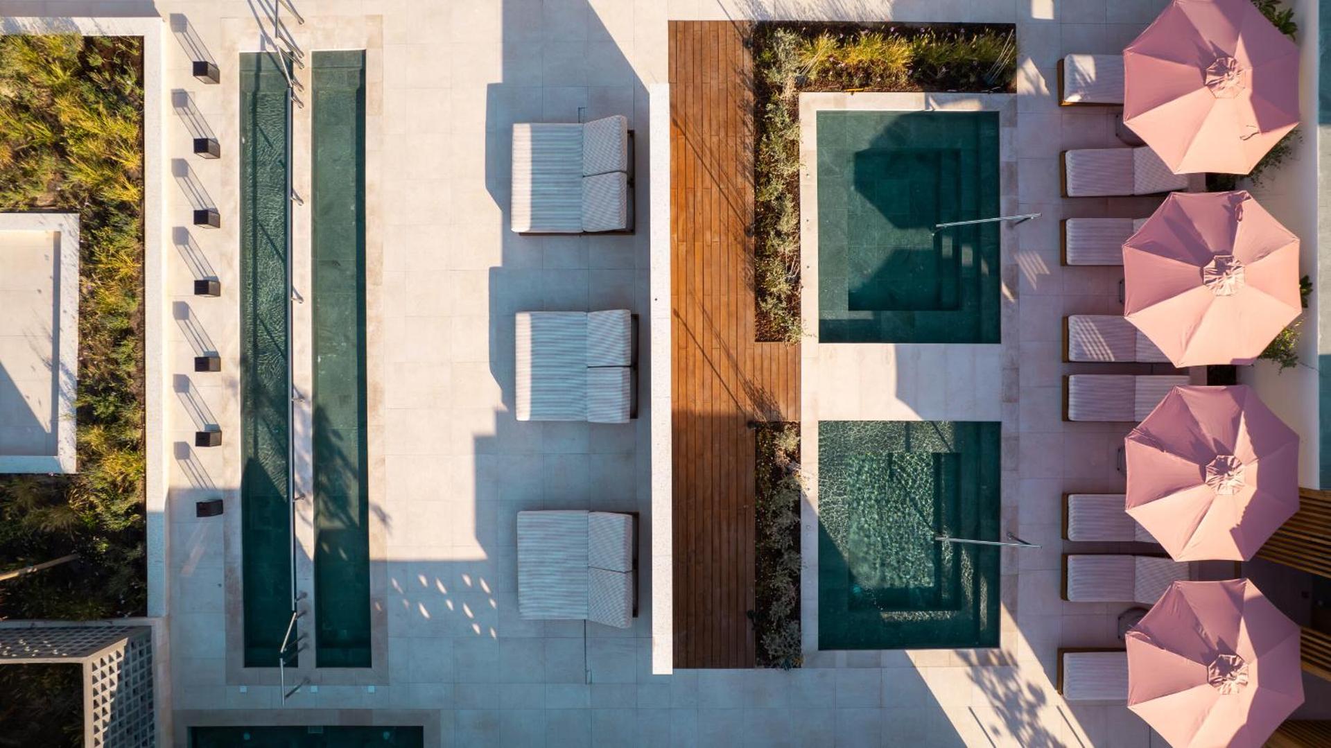 Mitsis Faliraki Beach Hotel & Spa skats no augšas uz modernu baseinu zonu ar rozā saulessargiem un ērtiem zviļņiem Rodas salā