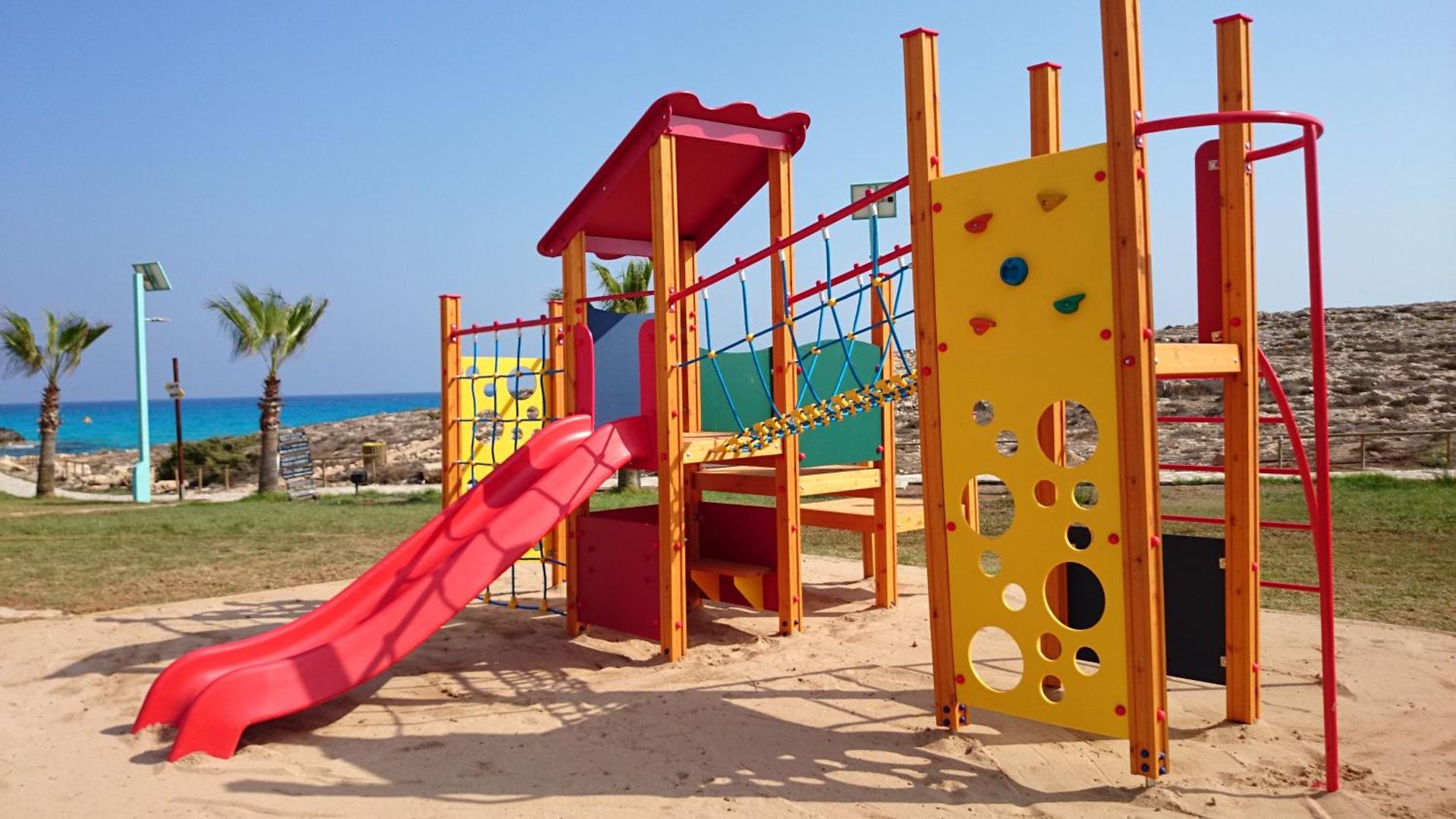 Bērnu rotaļu laukums ar slidkalniņu un kāpšanas sienu smilšu laukumā pie Aktea Beach Village viesnīcas un Vidusjūras krasta.