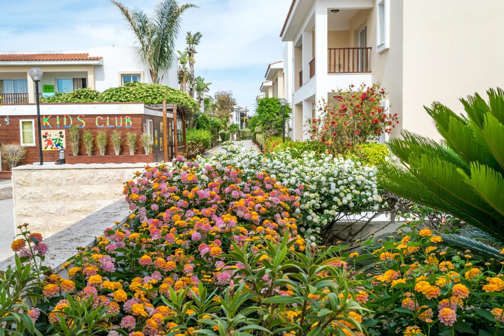 Aktea Beach Village teritorija ar ziedošiem krūmiem, bērnu klubu un divstāvu numuru ēkām dārza ielokā Ajanapā.