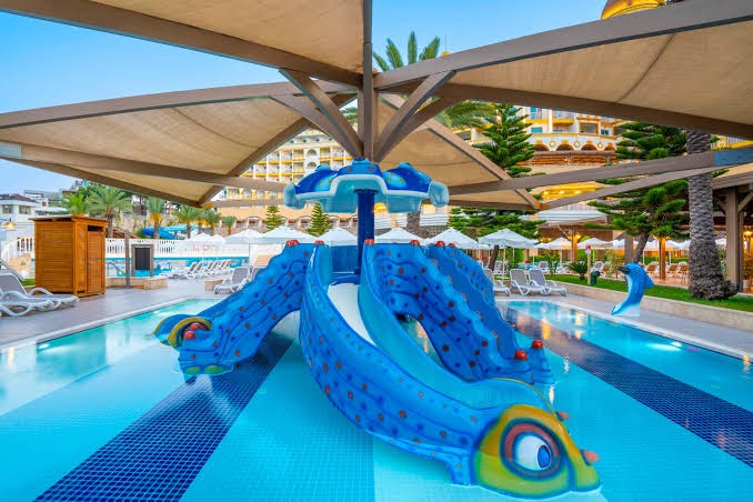 Kirman Sidemarin Beach & Spa bērnu baseins ar zilu slidkalniņu zivs formā un nojumi aizsardzībai pret sauli Turcijas piekrastē