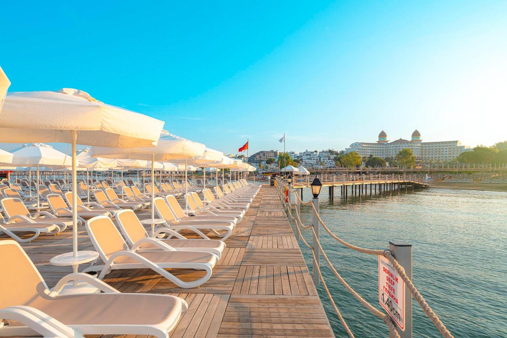 Kirman Sidemarin Beach & Spa koka laipa ar sauļošanās krēsliem un saulessargiem Vidusjūras piekrastē, Sidē, Turcijā — skats uz viesnīcas galveno ēku