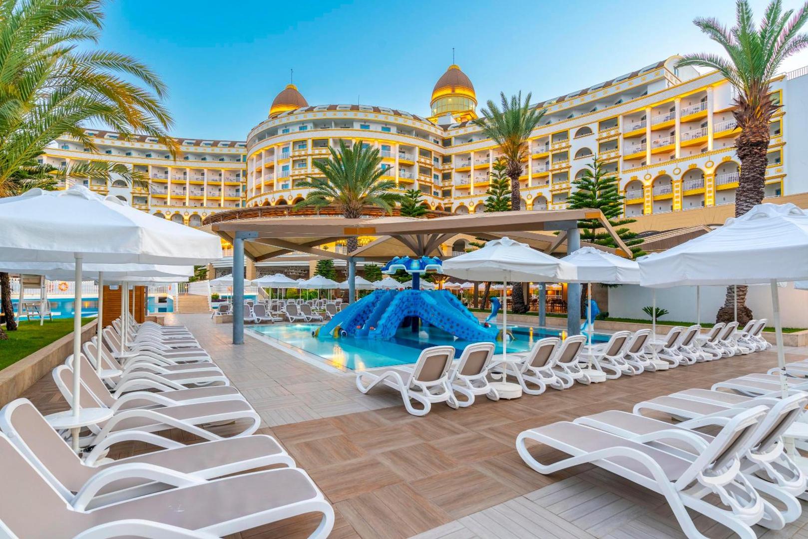 Kirman Sidemarin Beach & Spa viesnīcas ēka un galvenais baseins ar sauļošanās krēsliem, saulessargiem un palmām Sidē, Turcijā