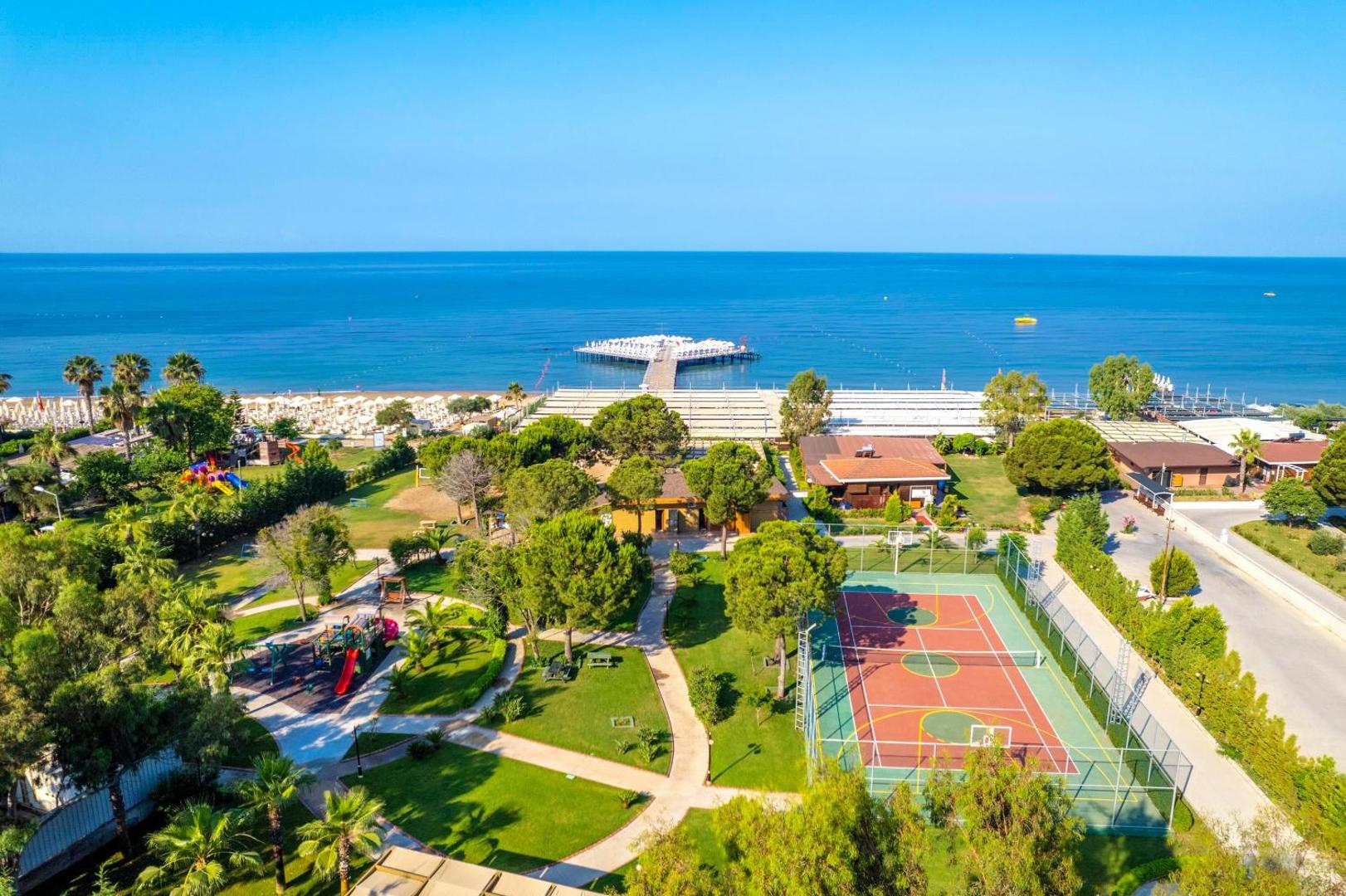 Kirman Sidemarin Beach & Spa teritorijas skats no augšas ar tenisa kortu, rotaļu laukumu un skatu uz Vidusjūru un piestātni