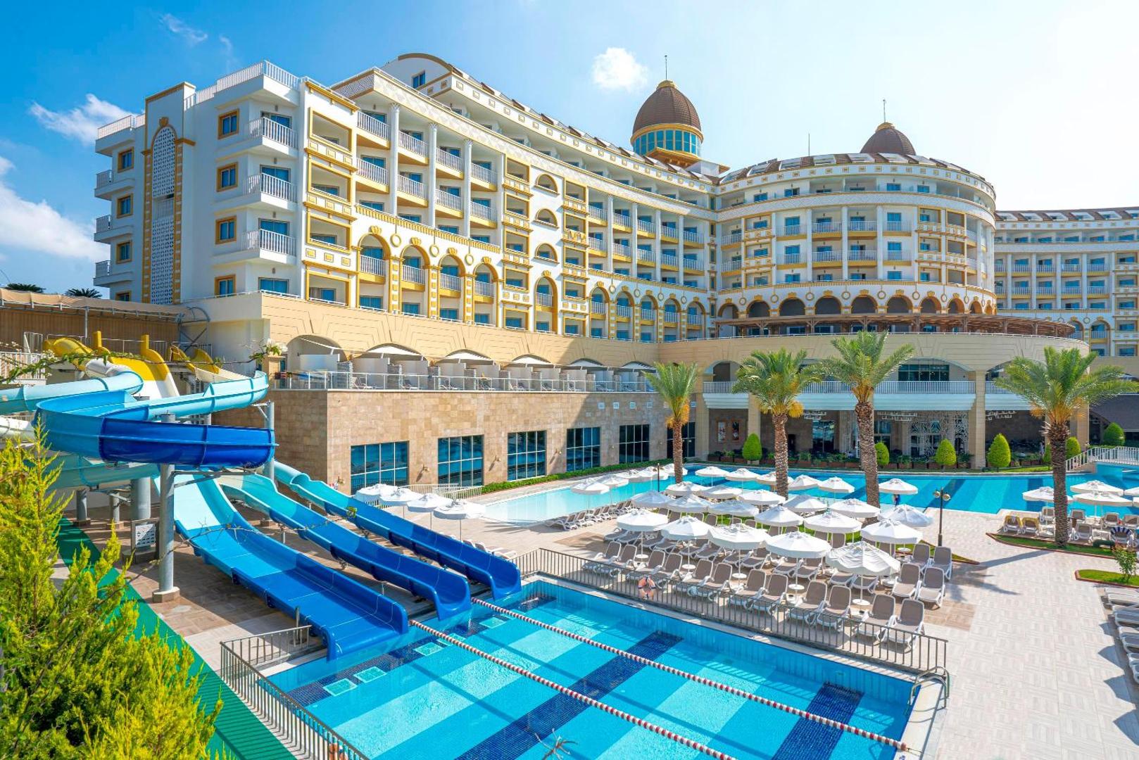 Kirman Sidemarin Beach & Spa akvaparka zona ar vairākiem zilajiem slidkalniņiem un bērnu baseinu pie viesnīcas fasādes