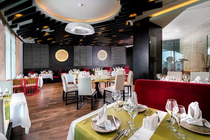 Kirman Sidemarin Beach & Spa a la carte restorāna interjers ar eleganti klātiem galdiem, sarkaniem dīvāniem un modernu griestu dizainu