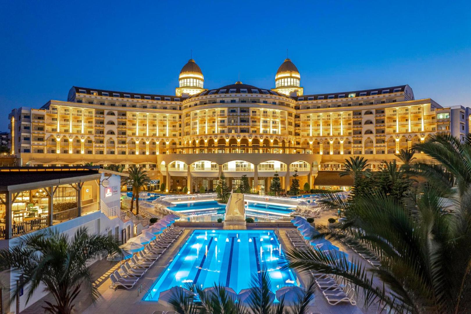 Kirman Sidemarin Beach & Spa viesnīcas galvenā ēka un izgaismotie āra baseini vakarā Sidē, Turcijā