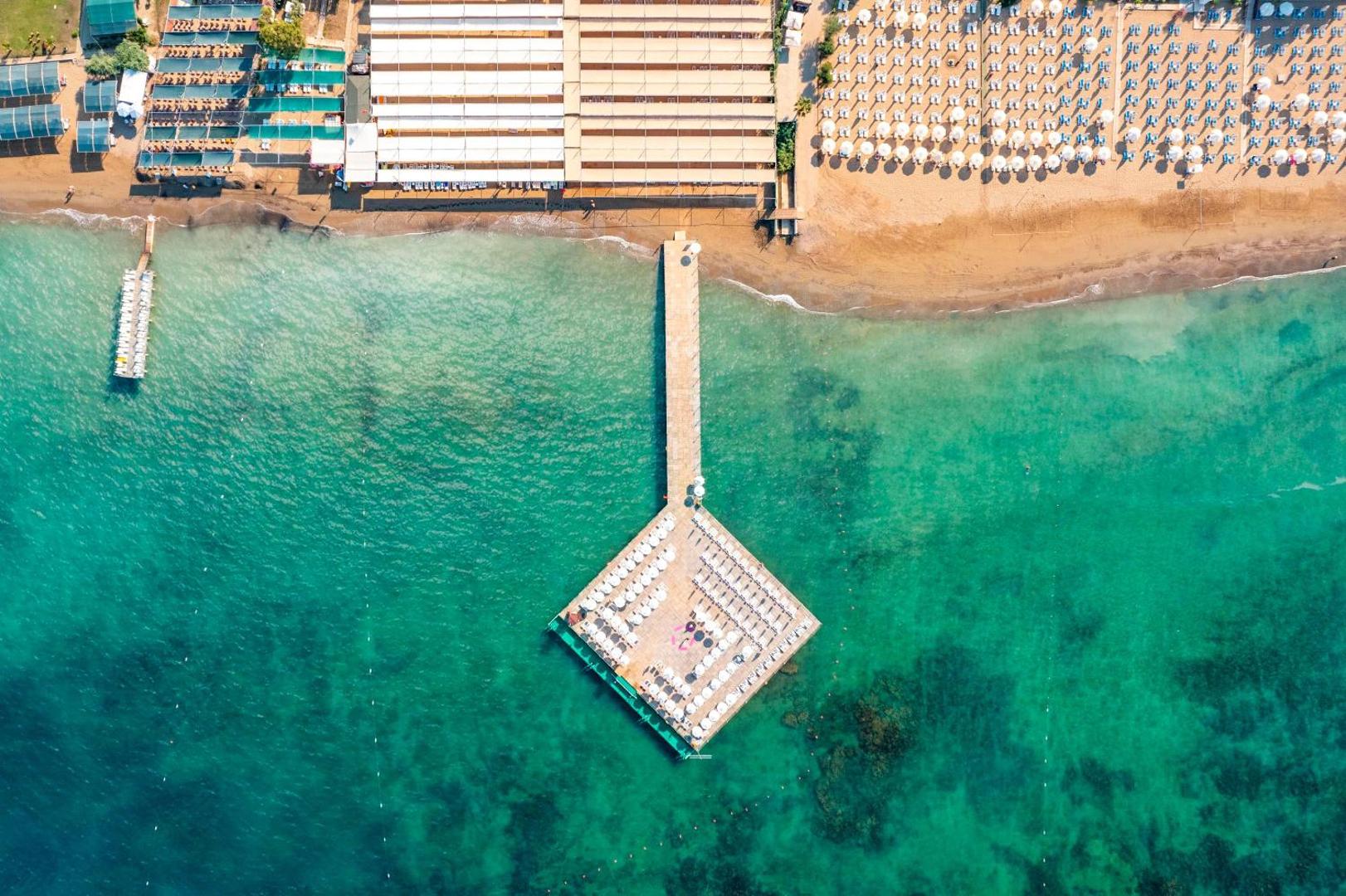 Kirman Sidemarin Beach & Spa skats no putna lidojuma uz pludmali un koka piestātni ar sauļošanās krēsliem tirkīzzilā ūdenī Sidē