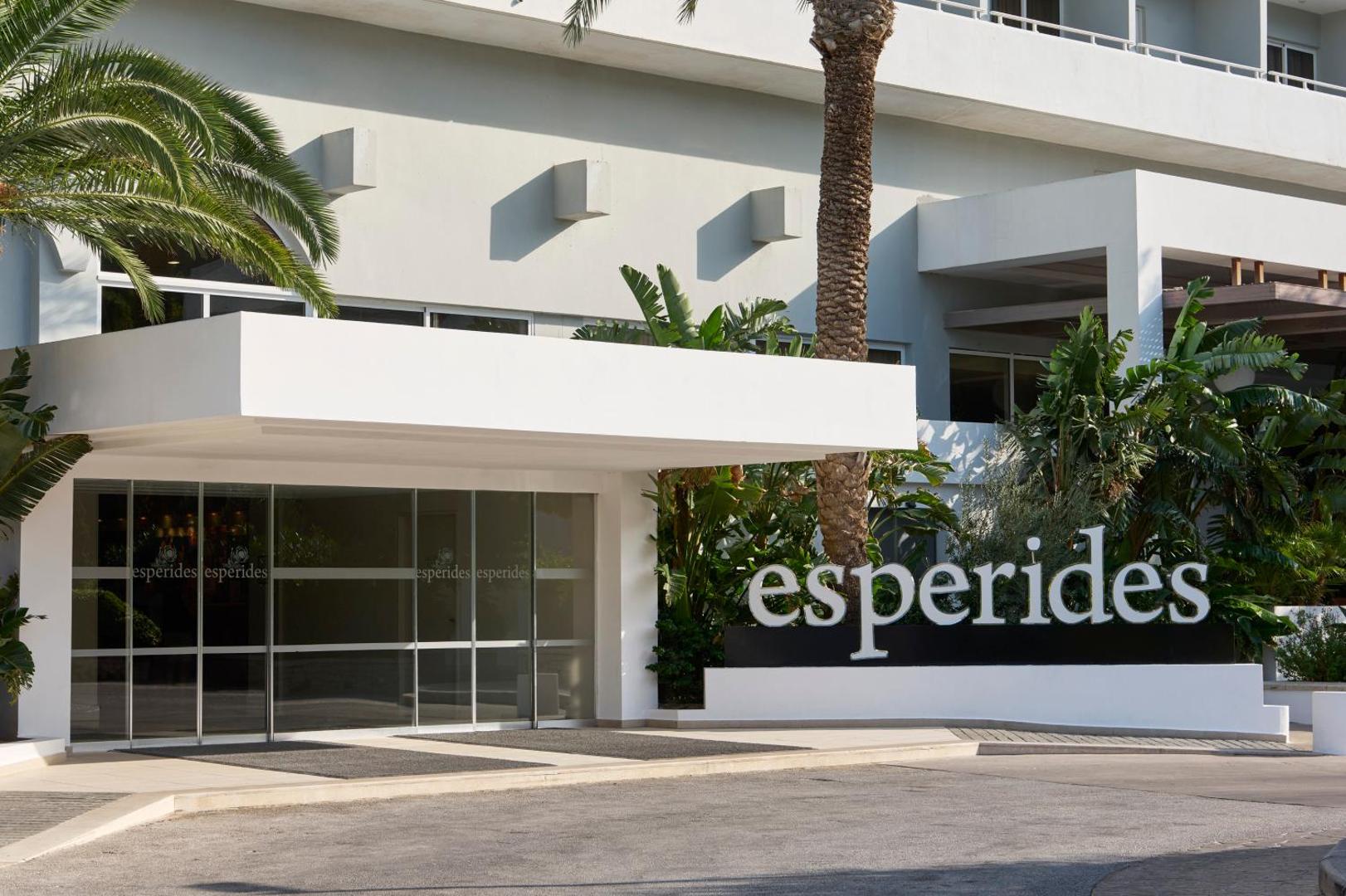 Esperides Beach viesnīcas galvenā ieeja ar nosaukuma zīmi, modernu stikla fasādi un eksotiskiem augiem Rodas kūrortā